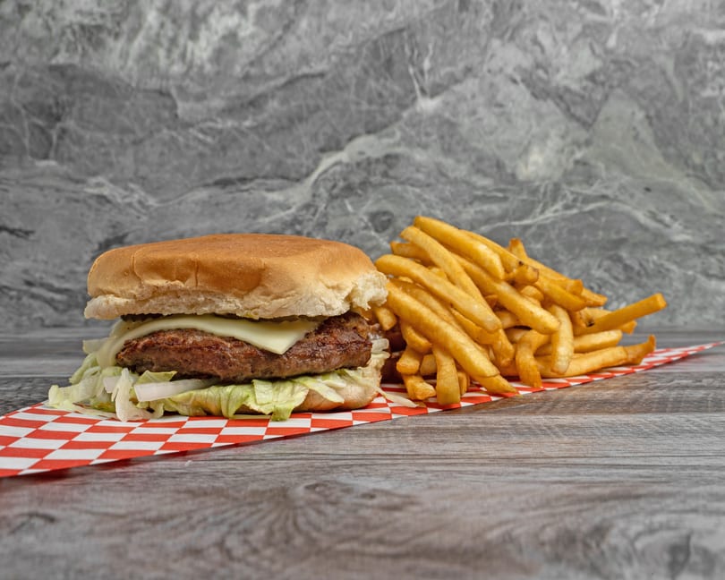 Cheeseburger with lettuce and onions, served with a side of golden french fries on a checkered paper.