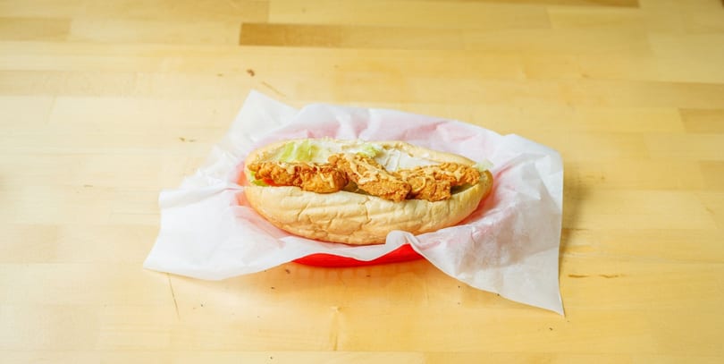 Crispy fried chicken sandwich with lettuce and sauce, served in a red basket on a wooden table.