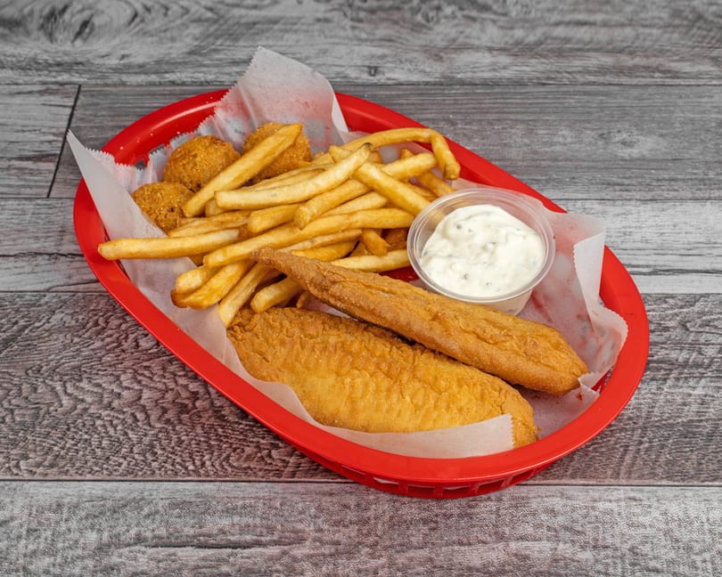 Fried fish fillets, hush puppies, and french fries with tartar sauce in a red basket.