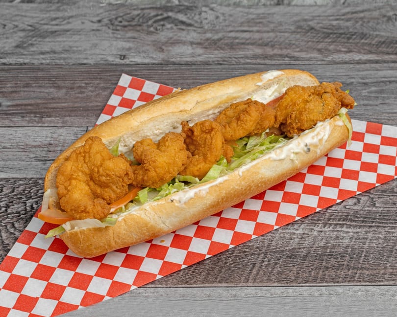 Crispy fried shrimp po'boy sandwich with lettuce, tomato, and mayonnaise on a red checkered paper.
