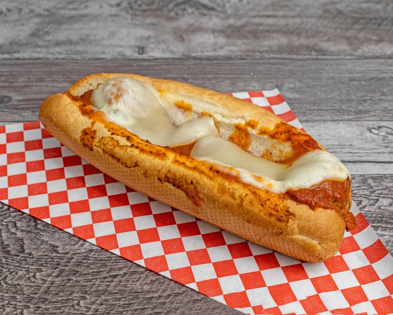 Meatball sub with melted mozzarella cheese and marinara sauce on a red and white checkered paper.