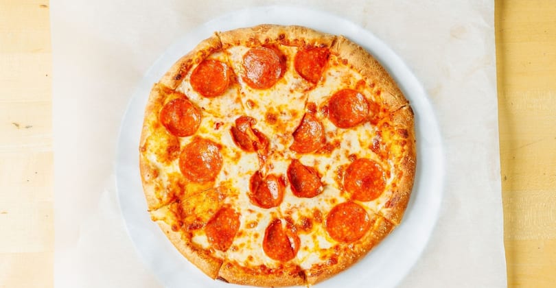 A whole pepperoni pizza, cut into slices, on a white plate and parchment paper.