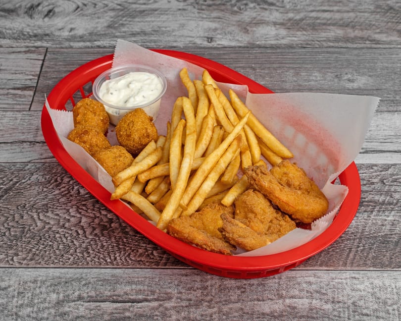 A red basket filled with golden-brown fried fish, hush puppies, french fries, and a side of tartar sauce.