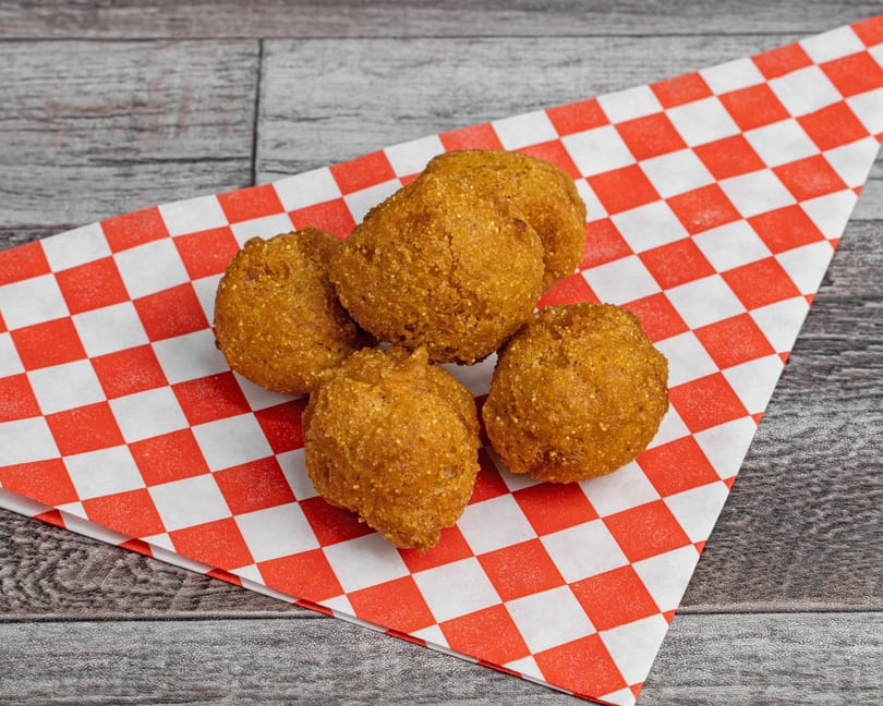 Five golden-brown hushpuppies rest on a red and white checkered paper on a wooden surface.
